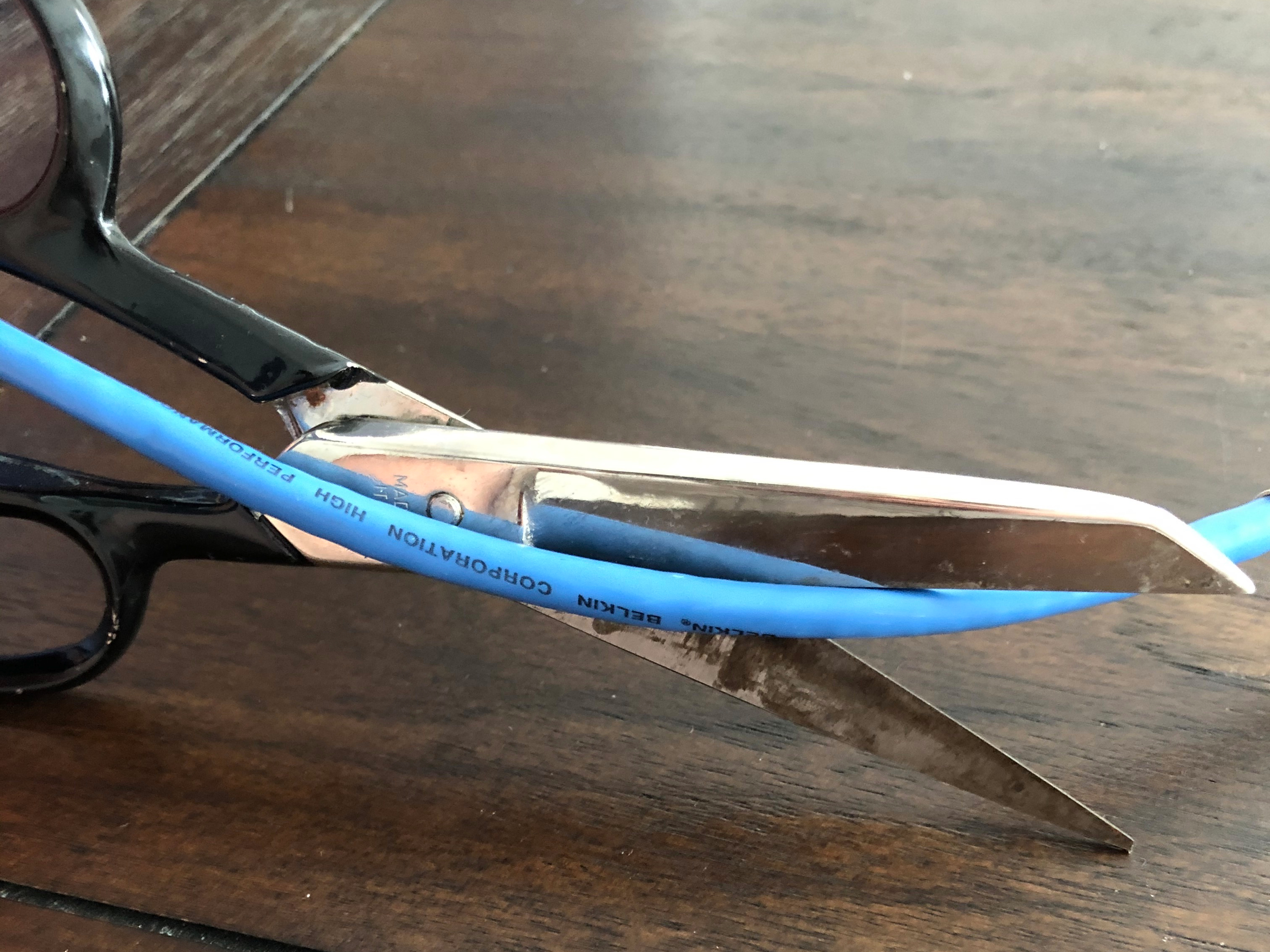 Tarnished scissors cutting through blue cable